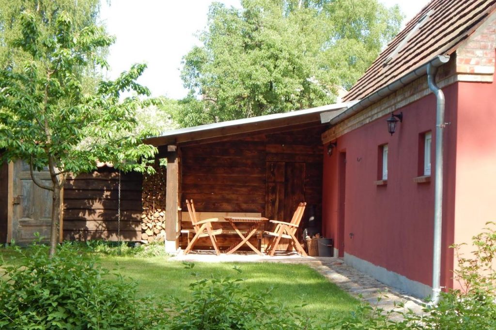 Überdachte Sitzecke mit Feuerholz im Garten des Ferienhauses mit Klavier